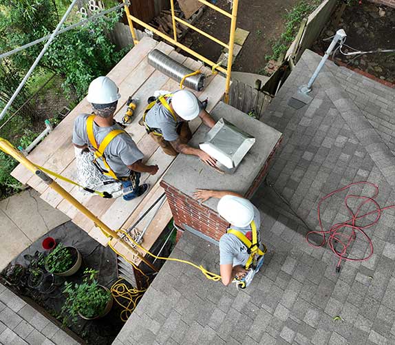 Overhead view of three men in hardhats and harnesses  installing a new chimney cap