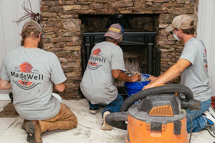 3 men kneeling on the ground and facing a fireplace with a vacuum bucket next to them
