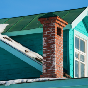 a masonry chimney on a blue-green house with snow surrounding on the rooftops